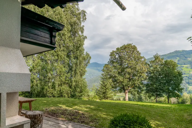Gemauerter Grill neben der Terrasse, dahinter Bäume und Berge