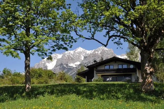 Das Haus zwischen alten Laubbäumen, dahinter der Dachstein
