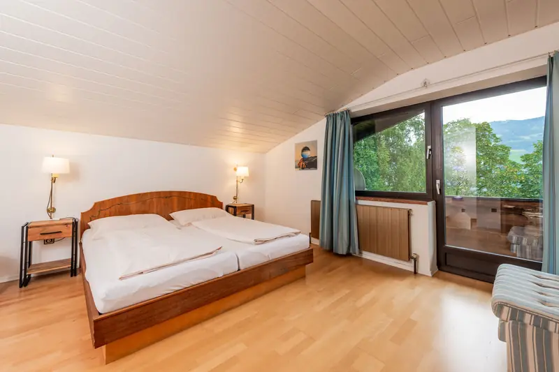 Schlafzimmer unter der Dachschräge mit Doppelbett und Balkontür