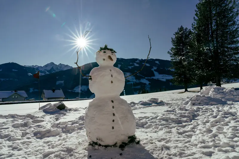 Schneemann auf der Wiese vor dem Haus, im Hintergrund die Berge